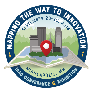 A city springs up from an illustrated map with a location marker in the center. Text reads: "Mapping the Way to Innovation. September 23-26, 2018. Minneapolis, MN. IAAO Conference & Exhibition."